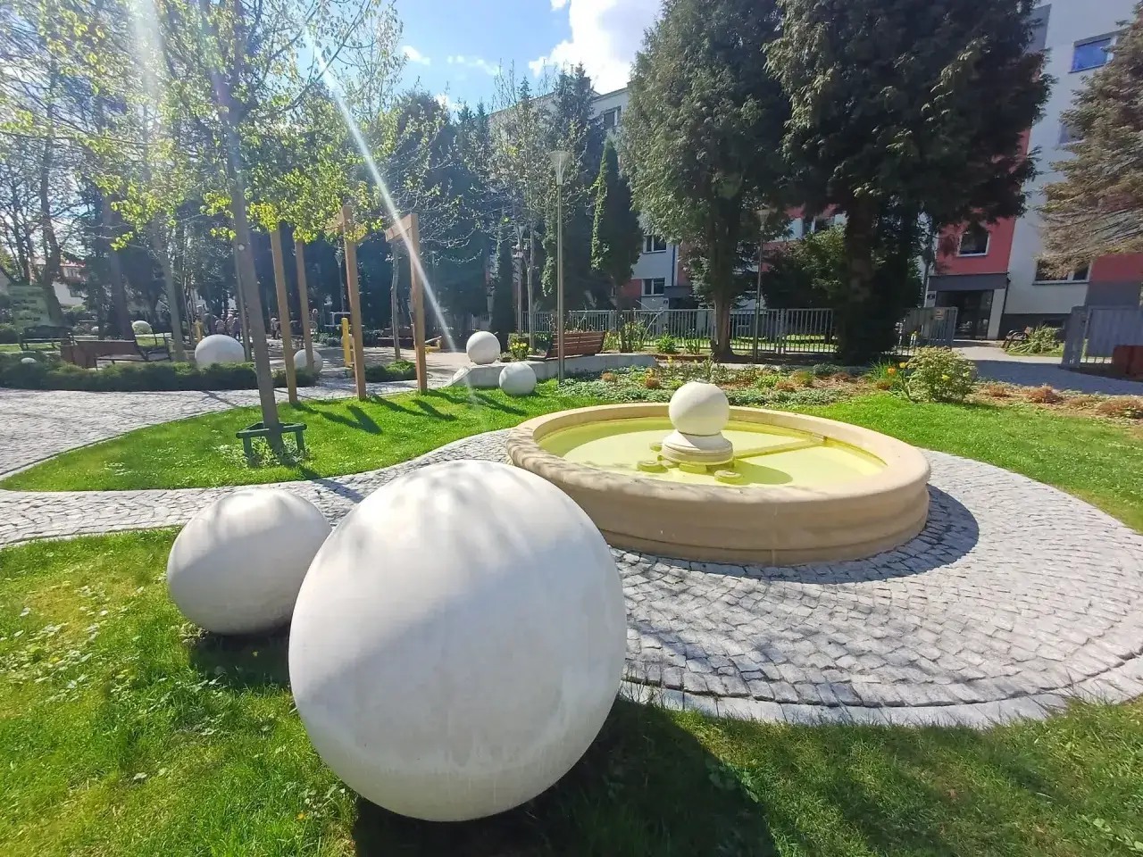 Nowe, nowoczesne ciechocinek atrakcje: fontanna i kamienne kule na tle zieleni i budynków.