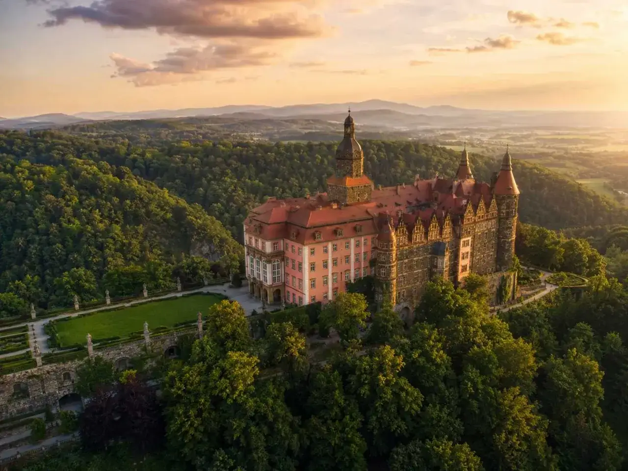 Zamek Książ w otoczeniu zielonych wzgórz, idealne miejsce na wycieczka jednodniowa śląskie. Zachód słońca maluje niebo na pomarańczowo.