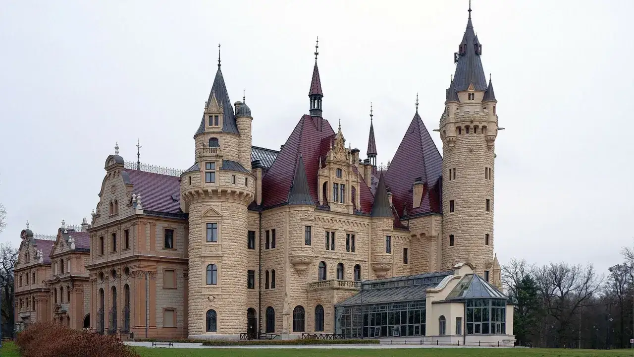 Zamek Książ, jeden z największych muzeów w Polsce, z licznymi wieżami i czerwonymi dachami, otoczony zielenią.
