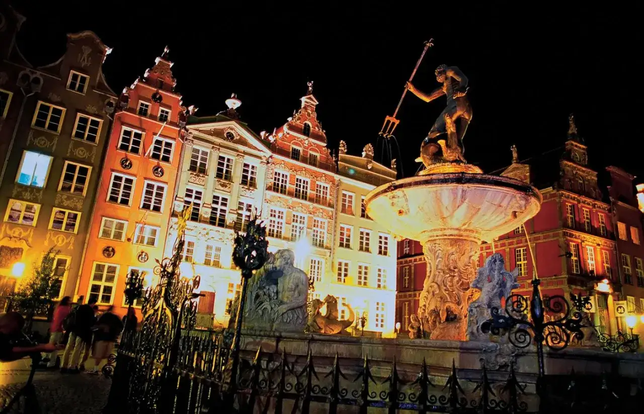 Gdańsk nocą, Fontanna Neptuna i zabytkowe kamienice rozświetlone blaskiem lamp.