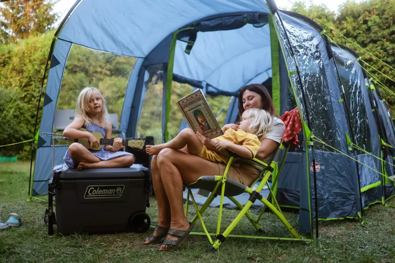 Co zabrać pod namiot z dziećmi? Książka, ukulele i lodówka Coleman to świetny początek. Rodzina relaksuje się pod namiotem.