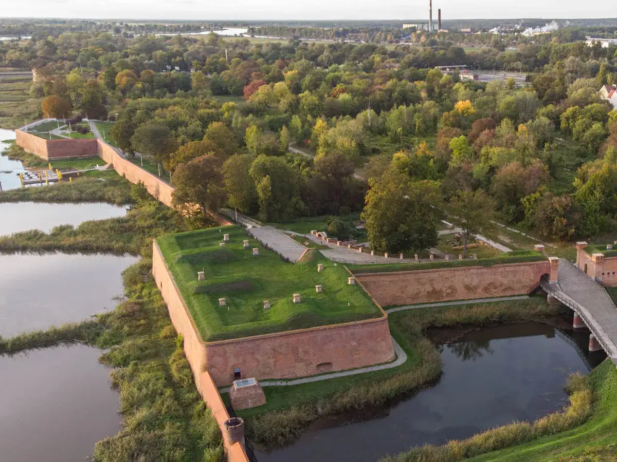 Fortyfikacje nad wodą, idealne na wycieczki jednodniowe lubuskie. Zieleń i cegła tworzą malowniczy krajobraz.
