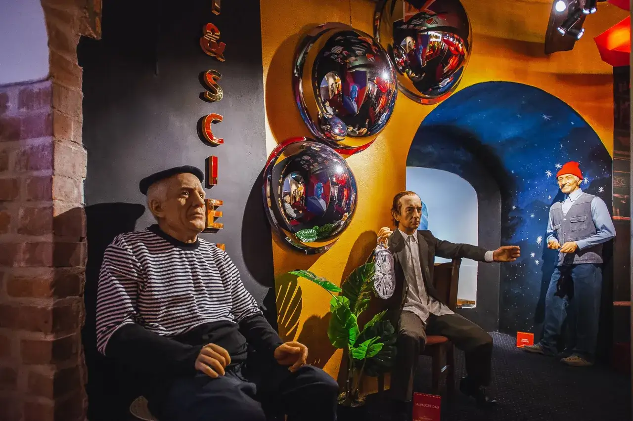 W muzeum figur woskowych Salvador Dalí trzyma zegar, a obok siedzi mężczyzna w beretce.