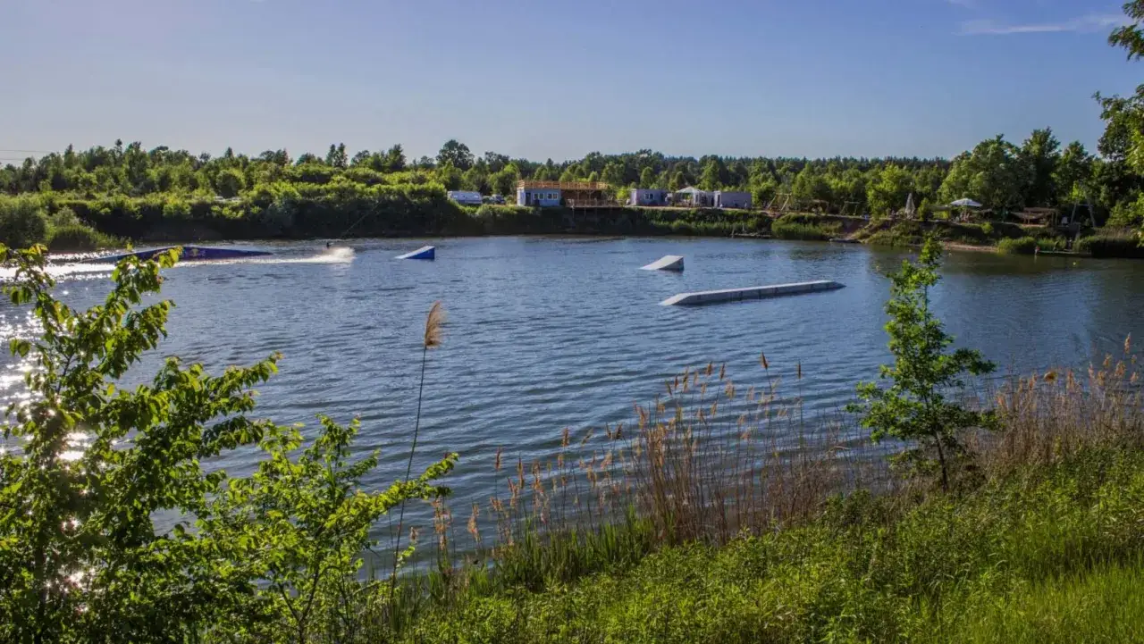 Jezioro Trzciańskie z przeszkodami do wakeboardingu. W oddali widać budynki i drzewa.