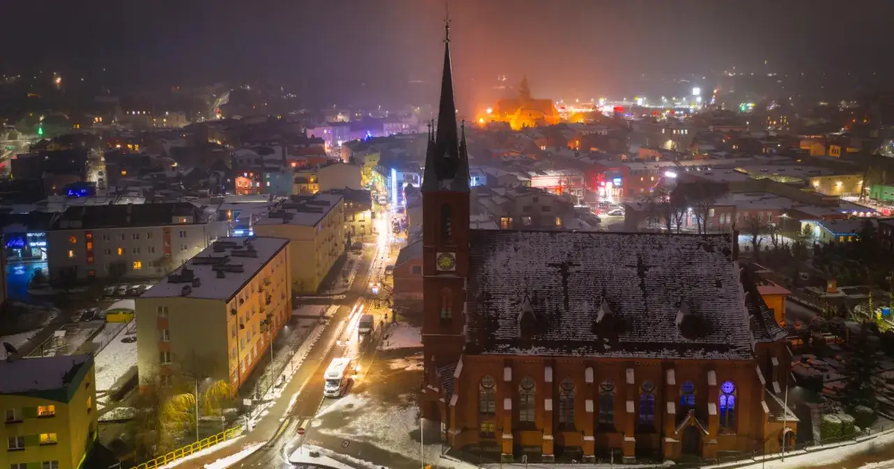 Wieczorny widok na Kościerzynę, gdzie ośnieżony kościół i rozświetlone budynki tworzą magiczną atmosferę. Odkryj kościerzyna atrakcje!