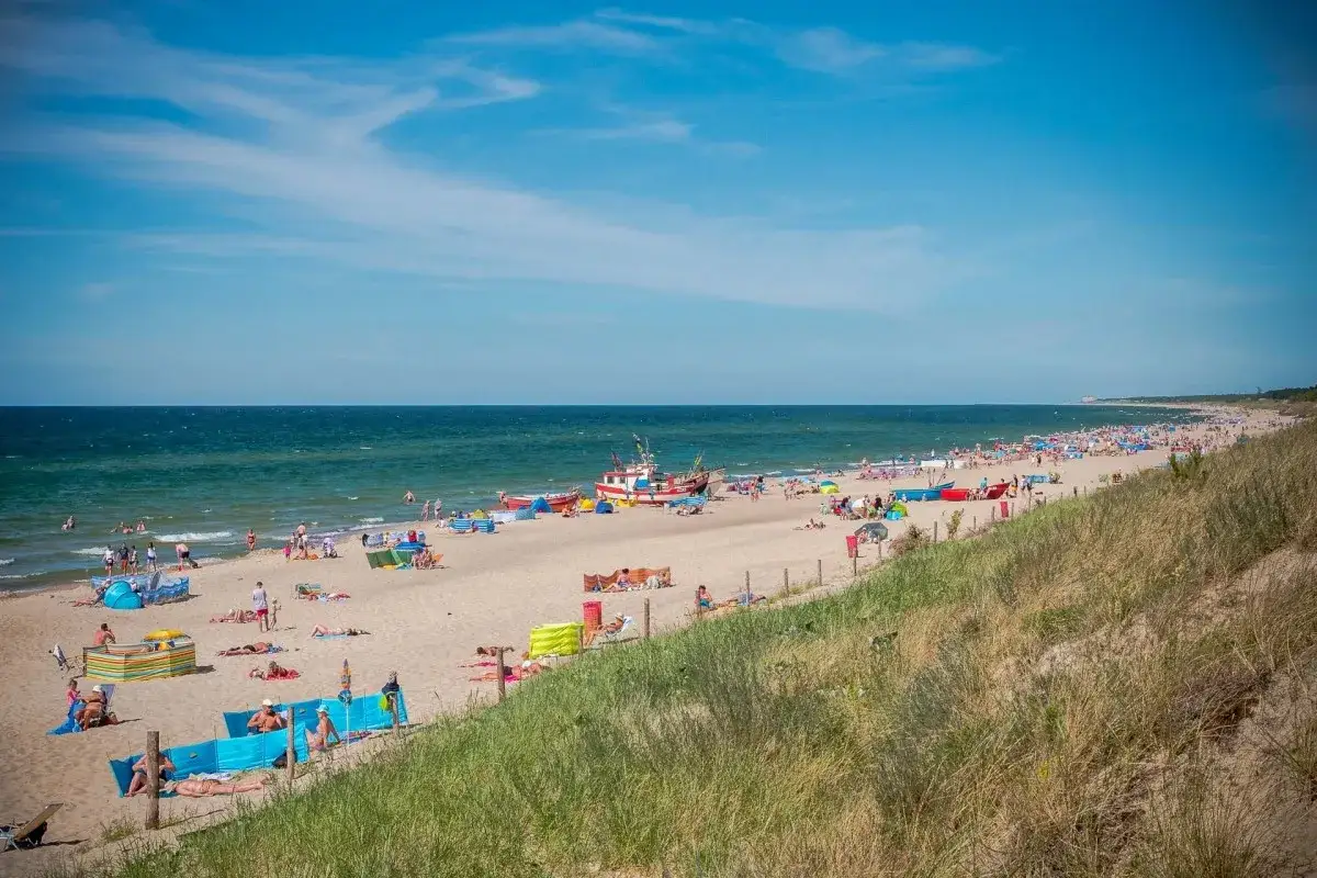 Słoneczna plaża w Dąbkach pełna turystów, kolorowych parawanów i łodzi. Idealne miejsce na wakacyjne atrakcje nad Bałtykiem.