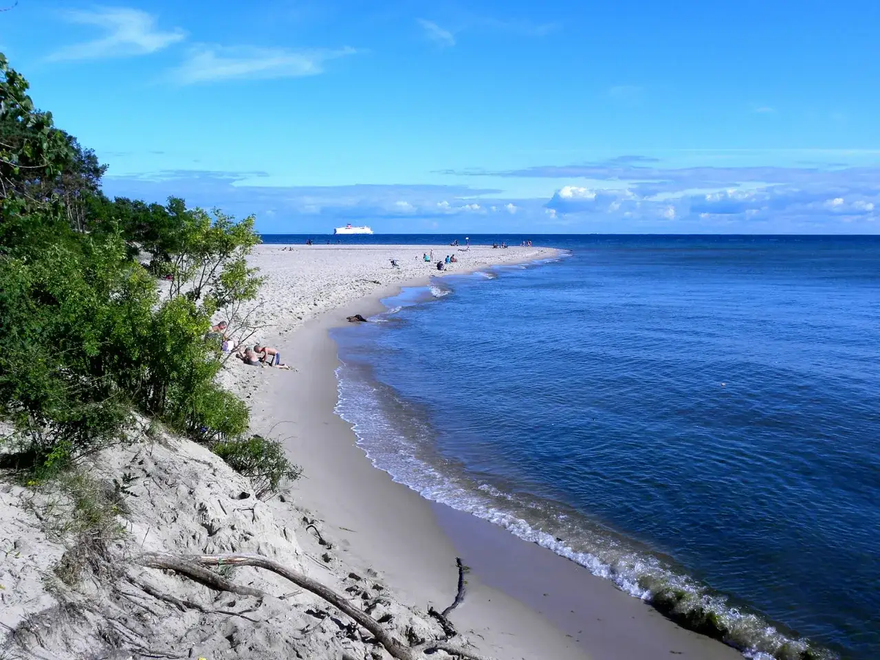 Piękna plaża nad Bałtykiem, przypominająca o urokach polskich miast portowych. W oddali widać statek.