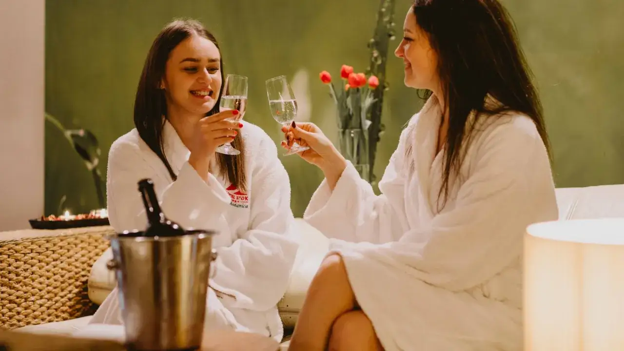 Dwie przyjaciółki w szlafrokach wznoszą toasty szampanem. Idealny weekend z przyjaciółką w spa.