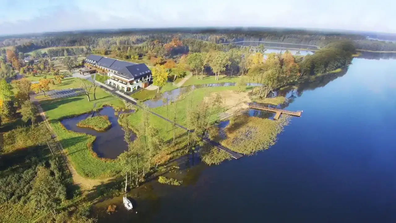 Malownicze Mazury blisko Warszawy: hotel nad jeziorem, otoczony jesiennym lasem, z pomostem i łódką.