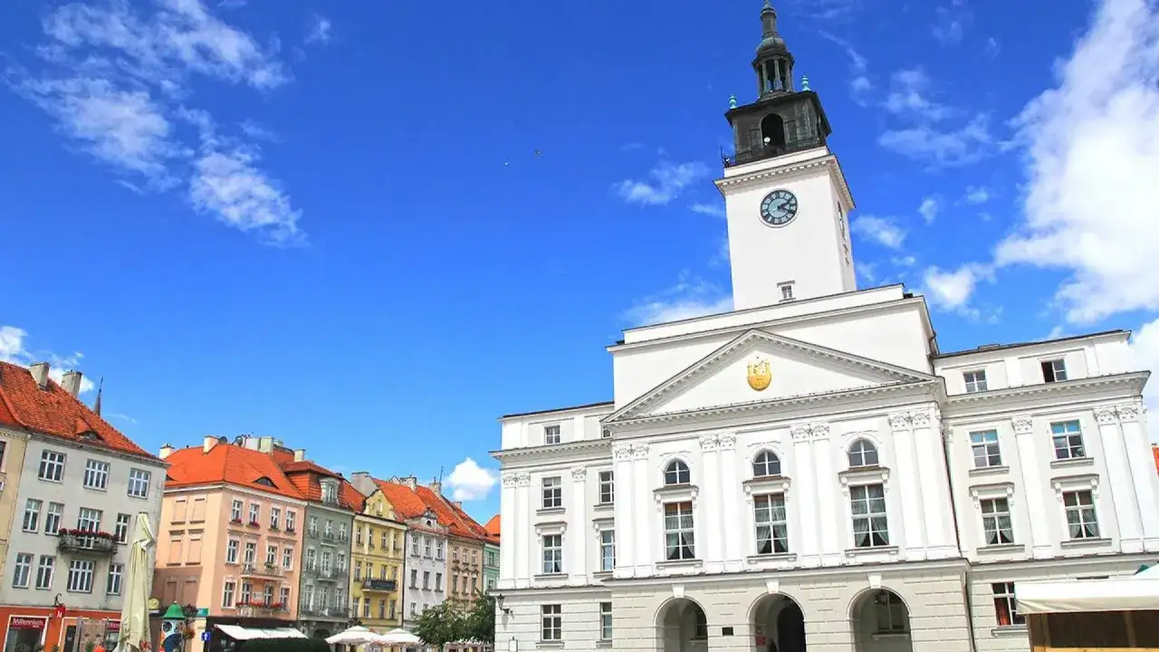 Rynek w Kaliszu, najstarszym mieście w Polsce, z ratuszem i kolorowymi kamienicami pod błękitnym niebem.