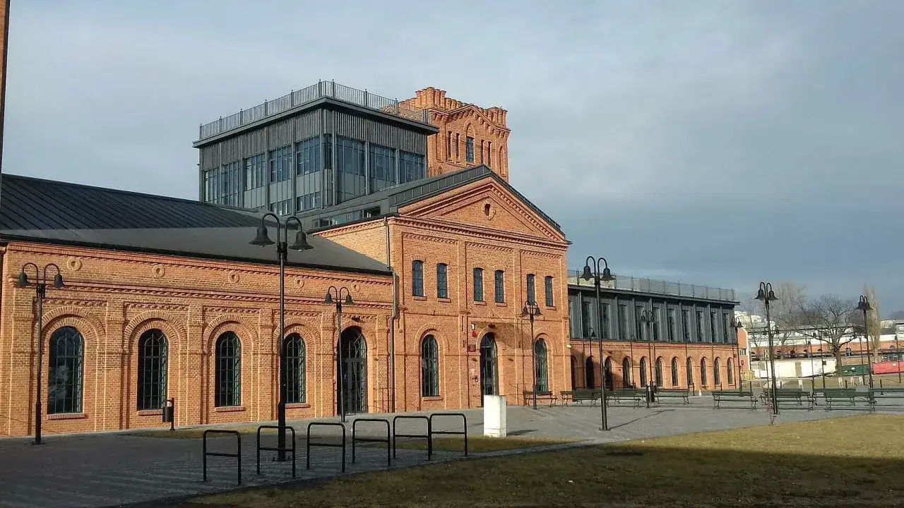 Ceglane budynki Księżego Młyna w Łodzi z nowoczesną dobudówką i wieżą.
