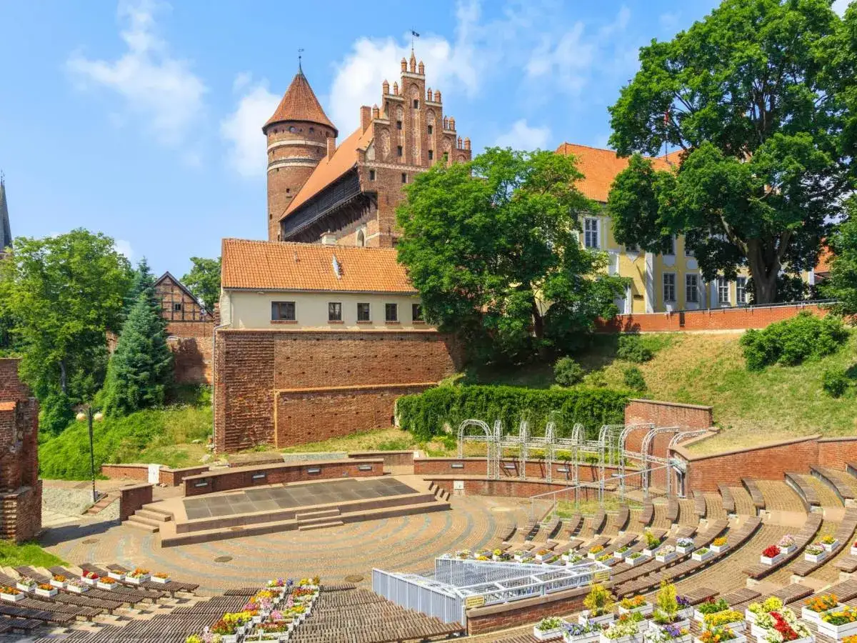 Amfiteatr i zamek w Olsztynie – wspaniałe olsztyńskie atrakcje. Widać tu kamienne mury, wieże i zielone drzewa.