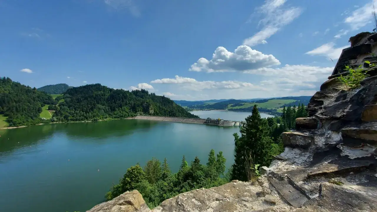 Malownicze jezioro w górach, otoczone zielonymi lasami, z tamą w oddali.