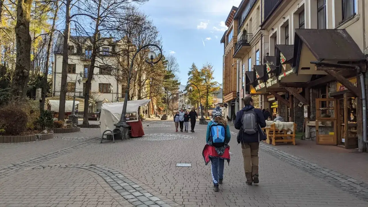 Spacer po Krupówkach w Zakopanem. Ludzie przechadzają się brukowaną ulicą, mijając kramy i góralskie karczmy.