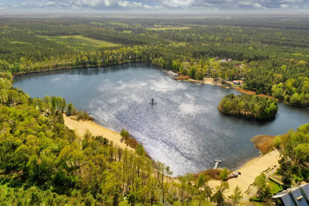 Malownicze jezioro opolskie otoczone lasem, z piaszczystymi plażami i małą wyspą.