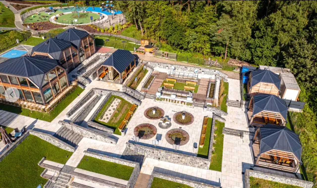 Nowoczesny park zdrojowy w Ciężkowicach z drewnianymi budynkami, placem zabaw i strefą relaksu.