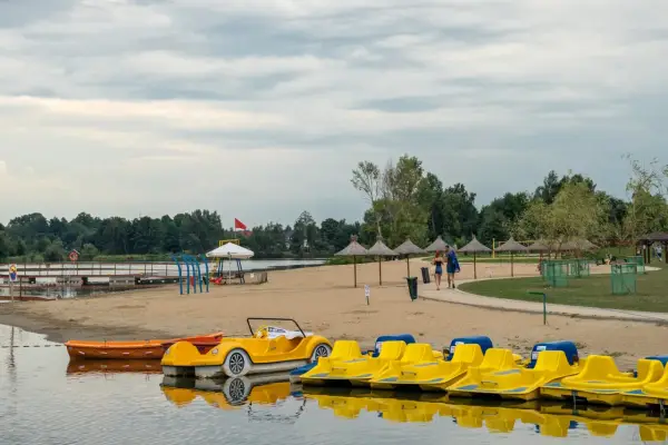 Plaża z żółtymi rowerami wodnymi i łódkami, idealna na weekendowy wypad na Mazury blisko Warszawy.