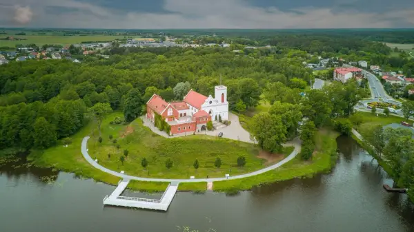 Zamek w Gostyninie, perła pojezierza gostynińsko-włocławskiego, wznosi się nad jeziorem, otoczony zielenią.