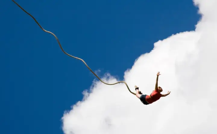 Osoba skacze na bungee, doświadczając jednych z najbardziej ekstremalnych atrakcji w Polsce. Wolny lot na tle błękitnego nieba i chmur.