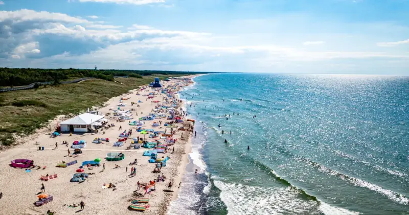 Tłum ludzi na plaży w Darłowie, korzystających z uroków lata. Wiele kolorowych parawanów i namiotów, a w wodzie kąpielowicze. To idealne darłowo atrakcje dla każdego.